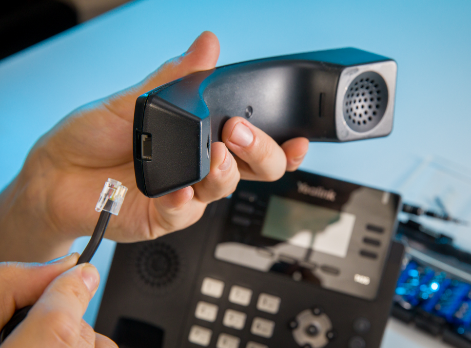 A pair of hands connecting a wire to a telephone handset.