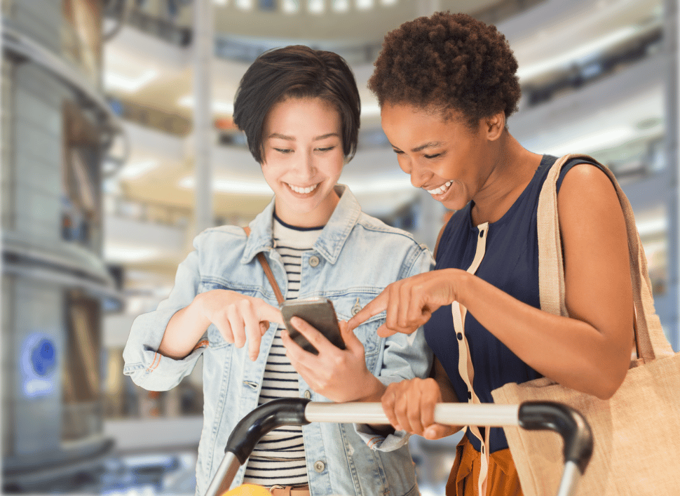 two women in shopping centre looking at phone