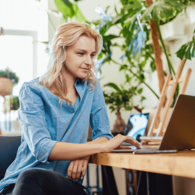 A woman with blonde hair and a blue shirt sitting sat a laptop.