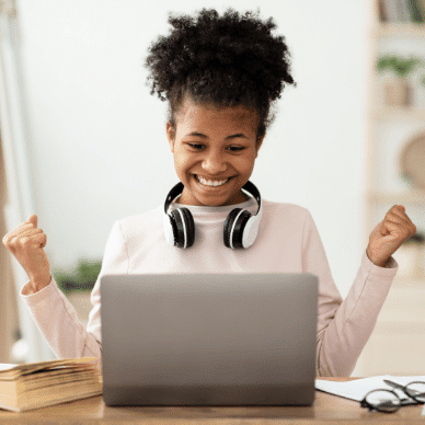 A young girl with head phones around her neck sitting at a laptop.